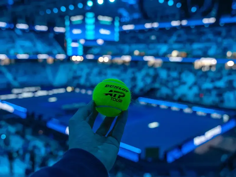 Tennis-Stadion aus Zuschauerperspektive mit Fokus auf einer Hand, die einen Tennisball hält