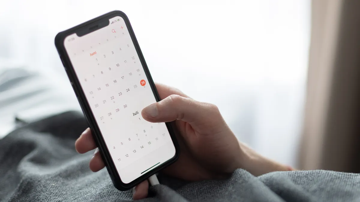 Smartphone mit Kalender auf dem Display, ein Datum ist ausgewählt.
