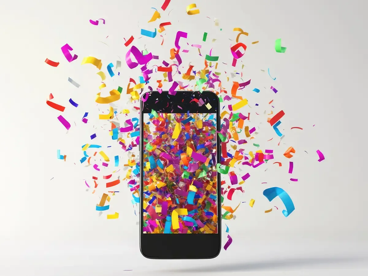 Schwarzes Smartphone vor grauem Hintergrund mit Konfetti auf dem Display und in der Luft