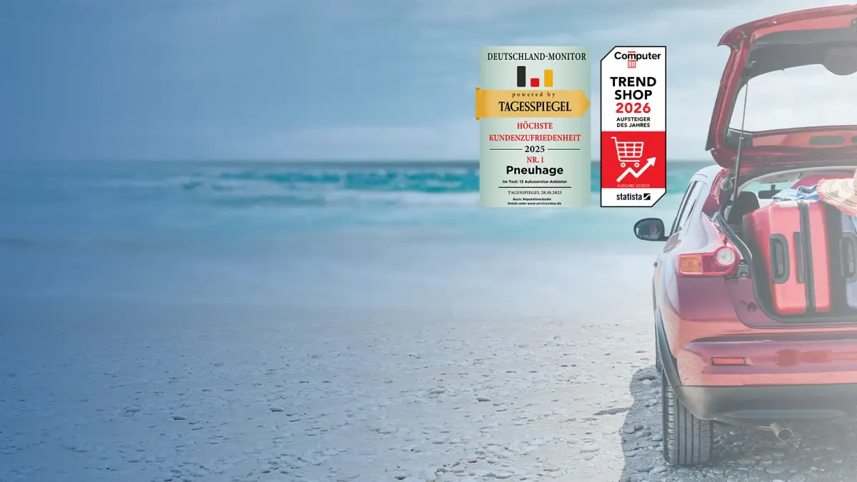 Rotes Auto mit geöffnetem Kofferraum und Gepäck an einem Strand, daneben zwei Testsieger-Auszeichnungen