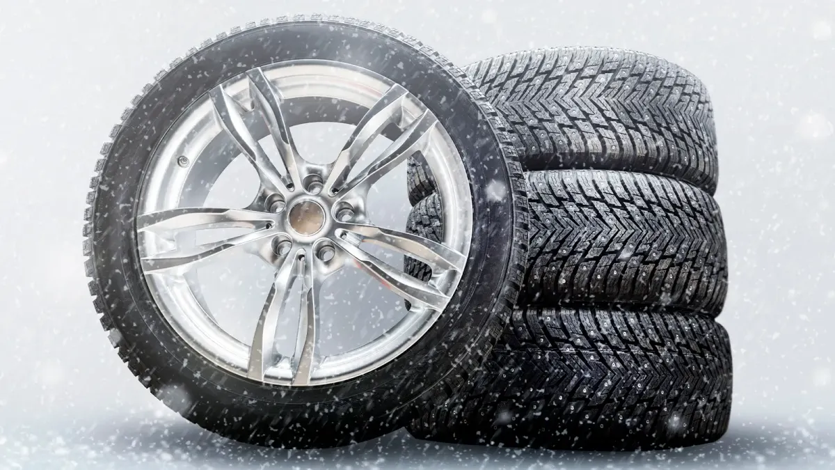 Satz neuer Winterreifen bei Schneefall – drei aufeinandergestapelt, einer daran angelehnt