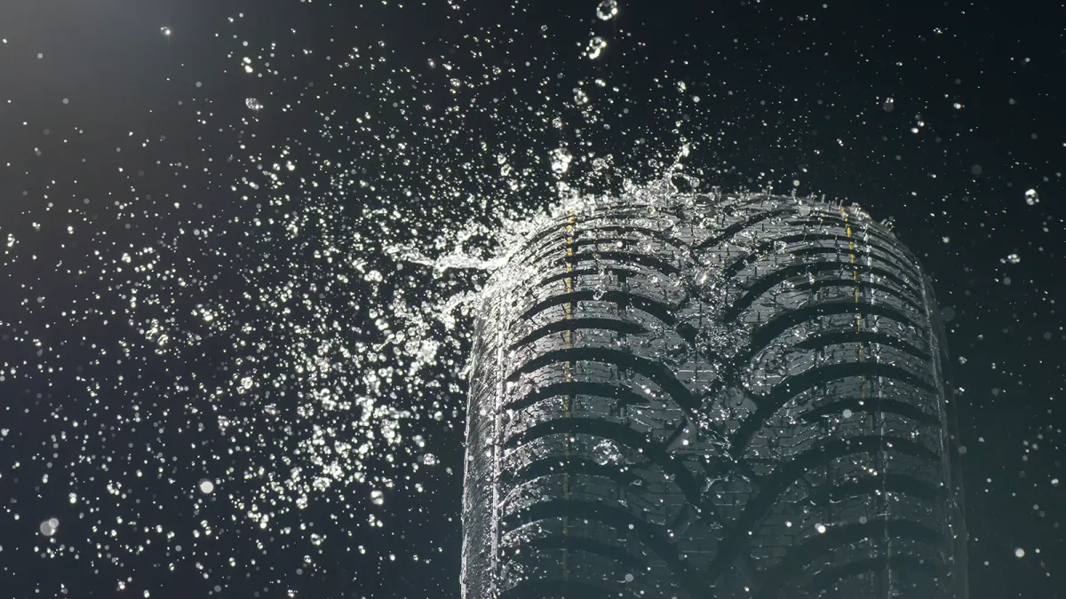 Detailaufnahme eines Reifens mit Profil, umgeben von aufspritzendem Wasser