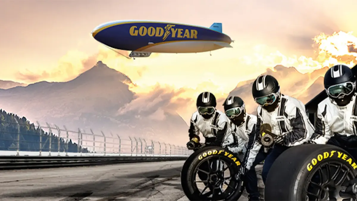 Mechaniker in Rennanzügen bereit zum Reifenwechsel in der Boxengasse, Goodyear-Luftschiff am Himmel im Hintergrund