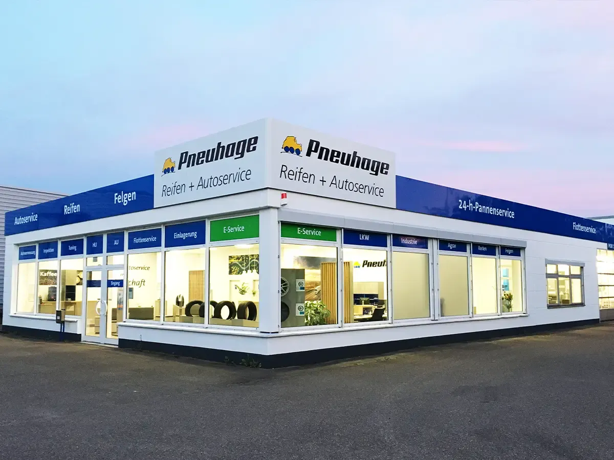 Nahaufnahme Pneuhage Reifen- und Autoservice-Filiale bei Dämmerung mit großen Schaufenstern und ausgestellten Reifen