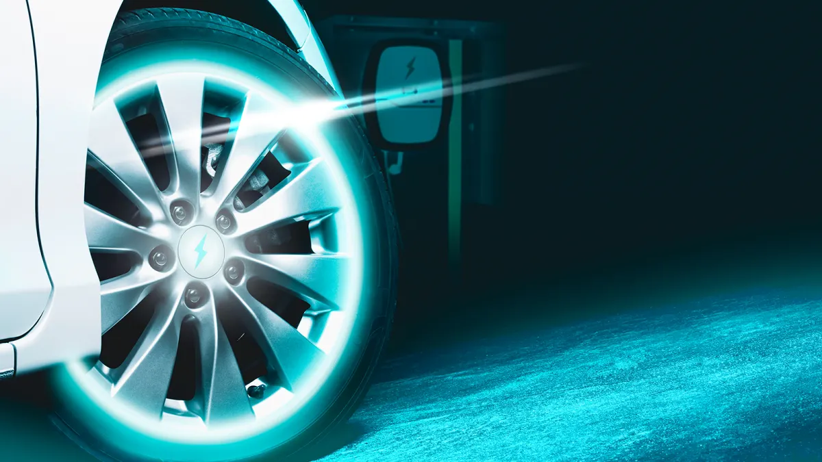 Vorderrad eines Elektrofahrzeugs vor einer unscharfen E-Ladestation in dunkler Umgebung