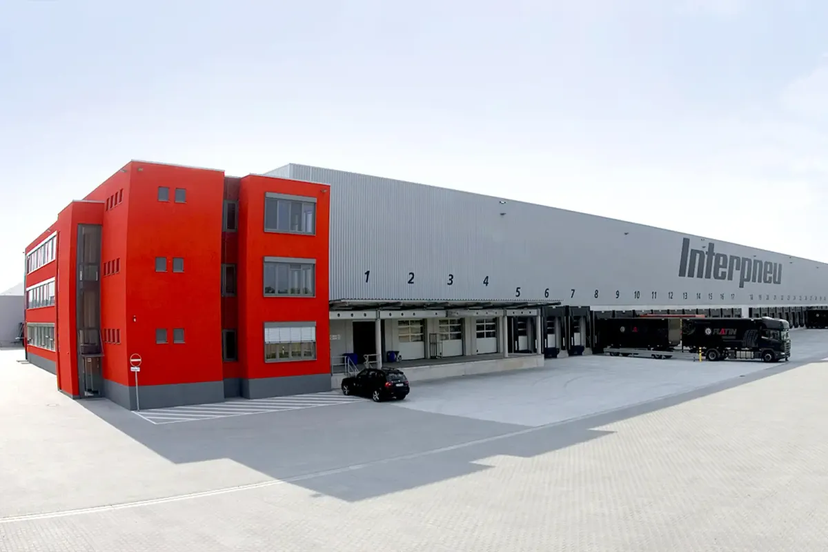 Modernes Logistikgebäude mit Interpneu-Schriftzug, Laderampen und geparkten Lastkraftwagen.