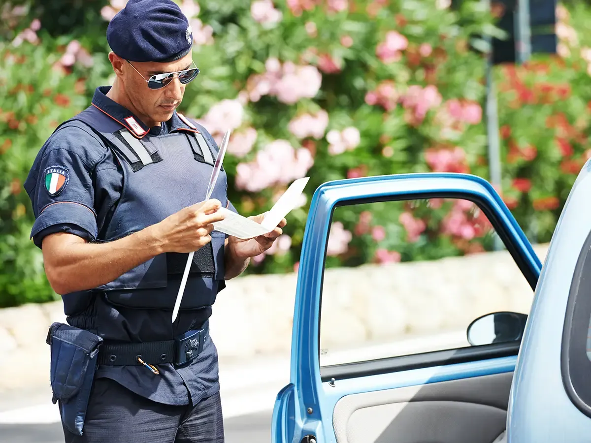 Uniformierter Polizeibeamter in Italien prüft Fahrzeugpapiere an der geöffneten Fahrertür