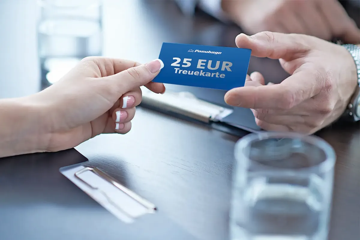 Eine Person überreicht einer anderen eine blaue Treuekarte mit 25-Euro-Guthaben