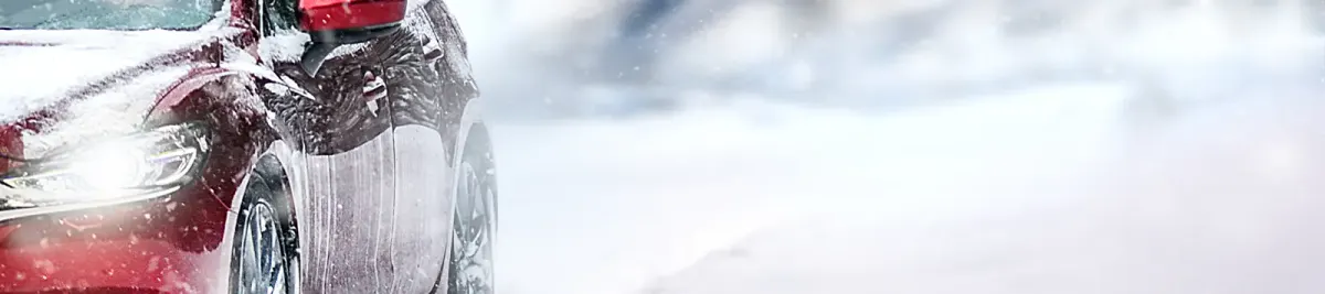 Blick von vorne auf eines roten Autos in Bewegung auf verschneiter Straße im Winter