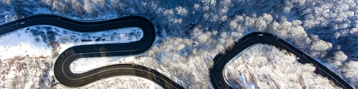 Luftaufnahme einer kurvigen Straße, die durch eine winterliche Waldlandschaft führt