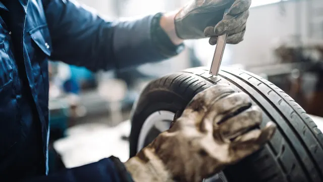 Messung der Reifenprofiltiefe von einem Mechaniker an einem Autoreifen in der Werkstatt