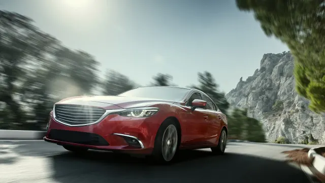 Rotes Auto fährt auf einer kurvenreichen Straße durch eine Berglandschaft
