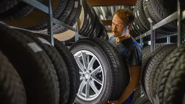 Bild Mitarbeiter lagert Autoreifen im Reifenlager und Kontrolliert diesen, mehrere verschiedene Reifenarten sind gelagert