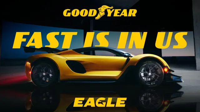 Sportwagen in Seitenansicht auf einer Bühne vor Goodyear Schriftzug und dem Slogan „FAST IS IN US“.