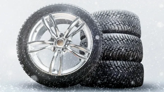 Satz neuer Winterreifen bei Schneefall – drei aufeinandergestapelt, einer daran angelehnt