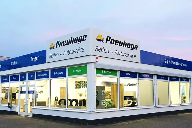 Nahaufnahme Pneuhage Reifen- und Autoservice-Filiale bei Dämmerung mit großen Schaufenstern und ausgestellten Reifen