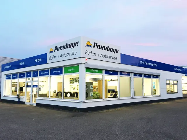 Nahaufnahme Pneuhage Reifen- und Autoservice-Filiale bei Dämmerung mit großen Schaufenstern und ausgestellten Reifen