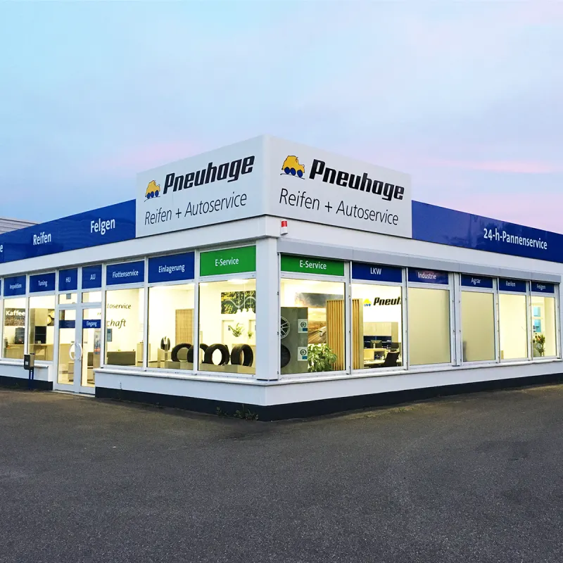 Pneuhage Reifen- und Autoservice-Filiale bei Dämmerung mit großen Schaufenstern und ausgestellten Reifen