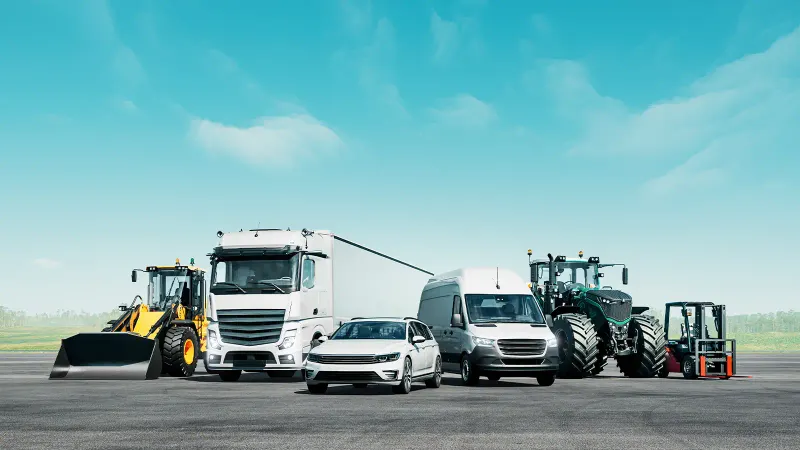 Verschiedene Fahrzeuge und Maschinen auf einer Freifläche, darunter Lkw, Transporter, Pkw und Traktor