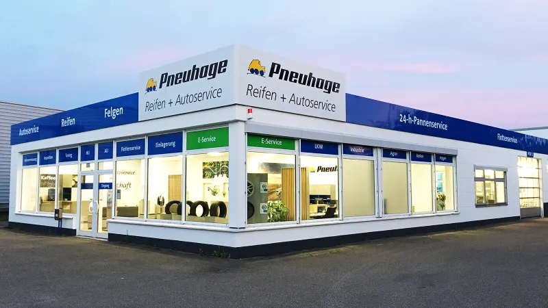 Pneuhage Reifen- und Autoservice-Filiale bei Dämmerung mit großen Schaufenstern und ausgestellten Reifen