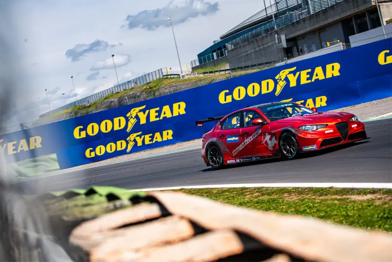 Roter Rennwagen fährt auf einer Rennstrecke, Goodyear-Bandenwerbung im Hintergrund