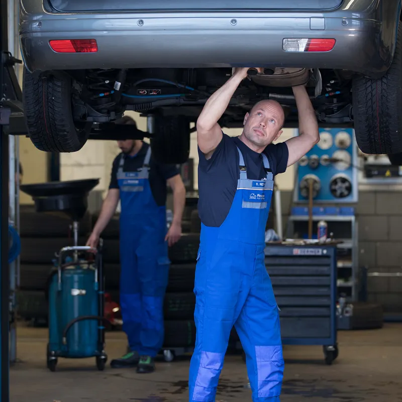 Mechaniker prüft Auspuffanlage unter einem Fahrzeug auf der Hebebühne